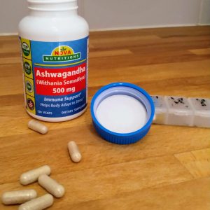 An open jar of Ashwaghanda supplement capsules, with some capsules spread across the table